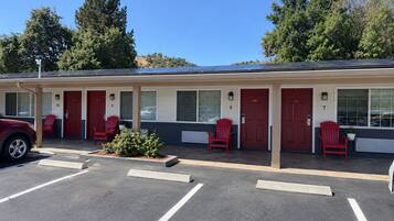 Un motel con habitaciones numeradas, puertas rojas y un estacionamiento.
