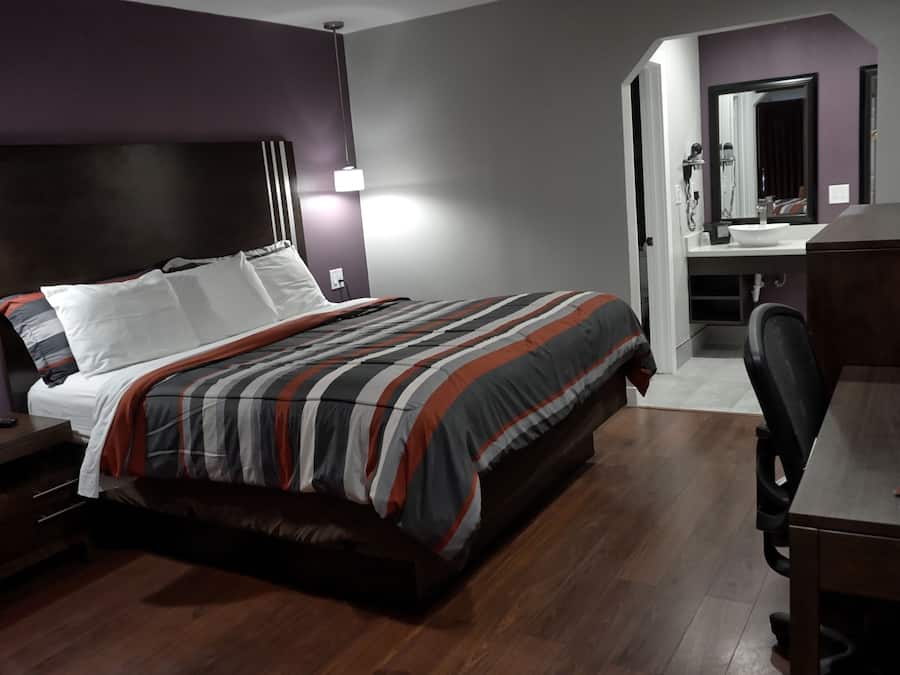 A hotel room with a bed, a desk, a chair, a mirror, and a bathroom visible through an open door.