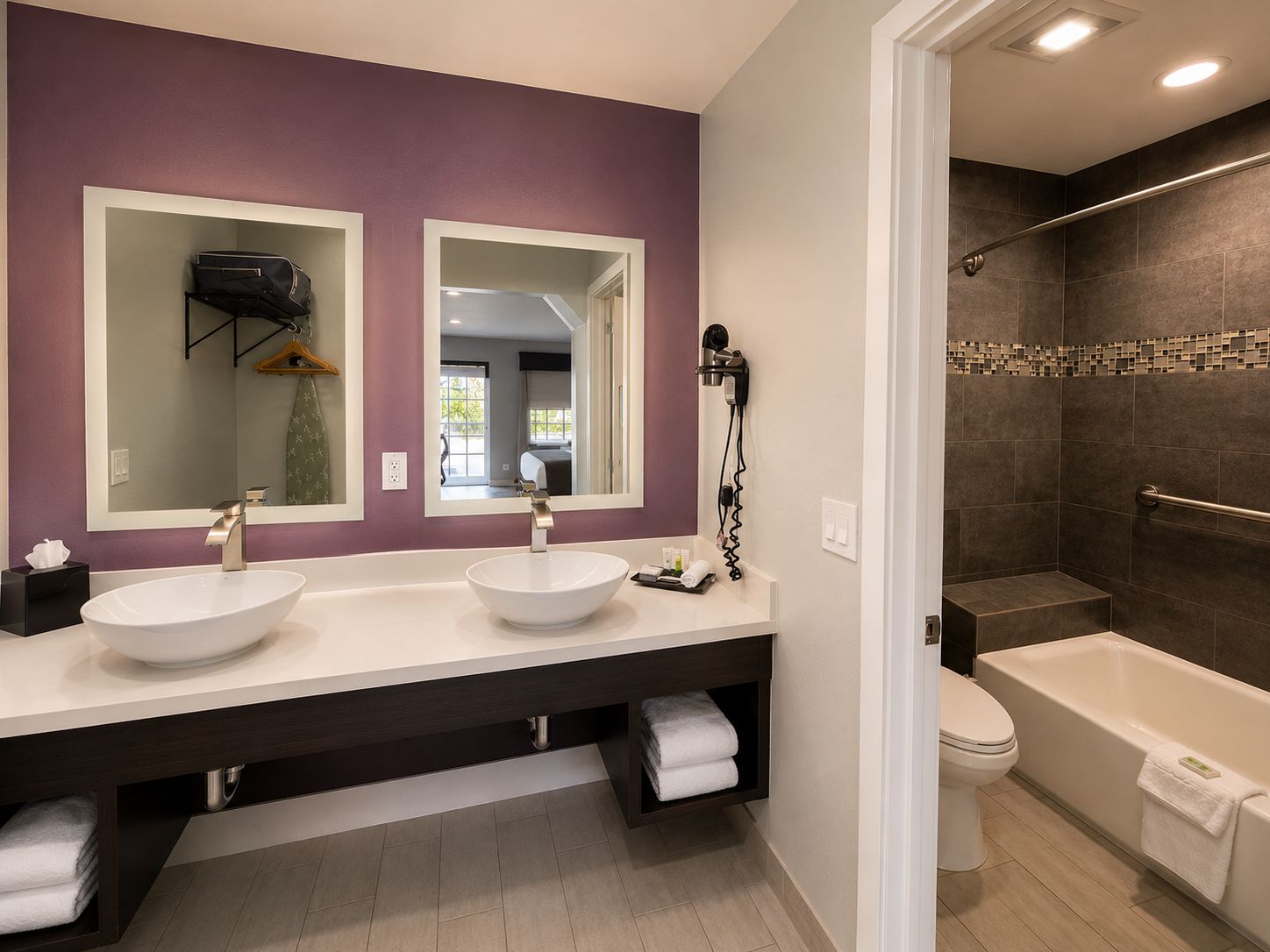 A modern bathroom with a double sink vanity, a large mirror, a hairdryer, a walk-in shower, and a toilet.