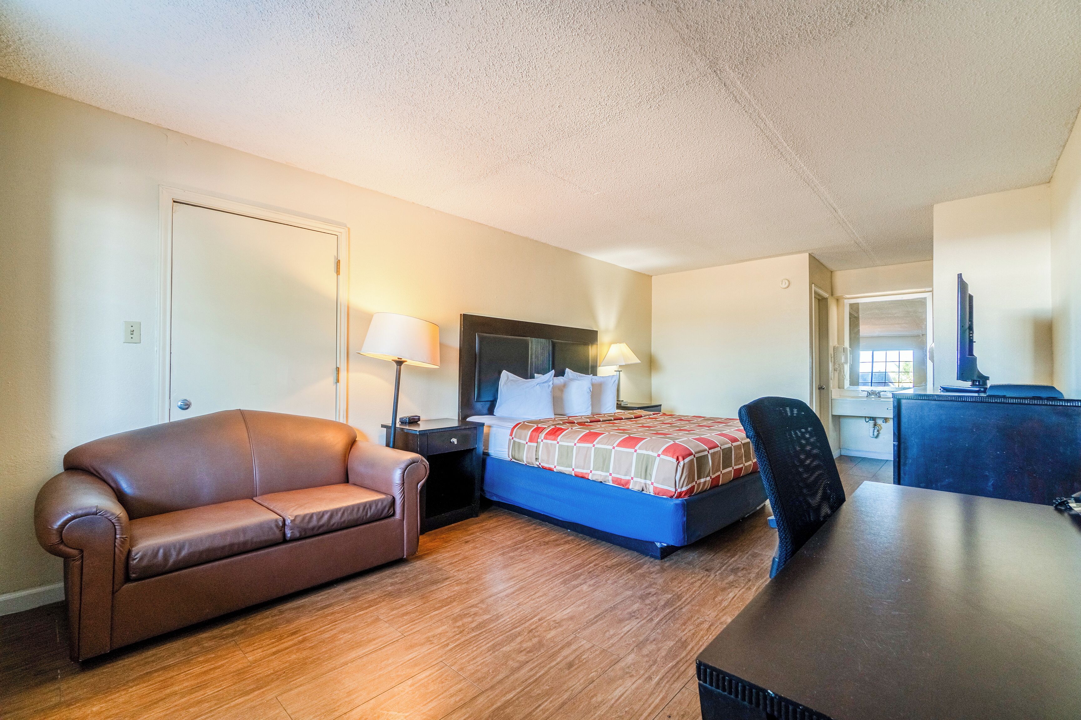 A hotel room with a bed, a desk, a chair, a couch, and a nightstand with lamps.