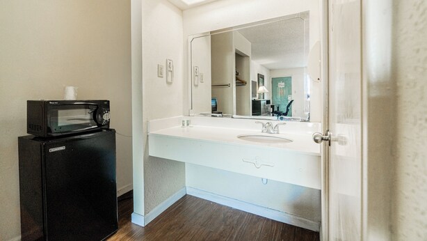 A bathroom with a white sink, a large mirror, and a black refrigerator.