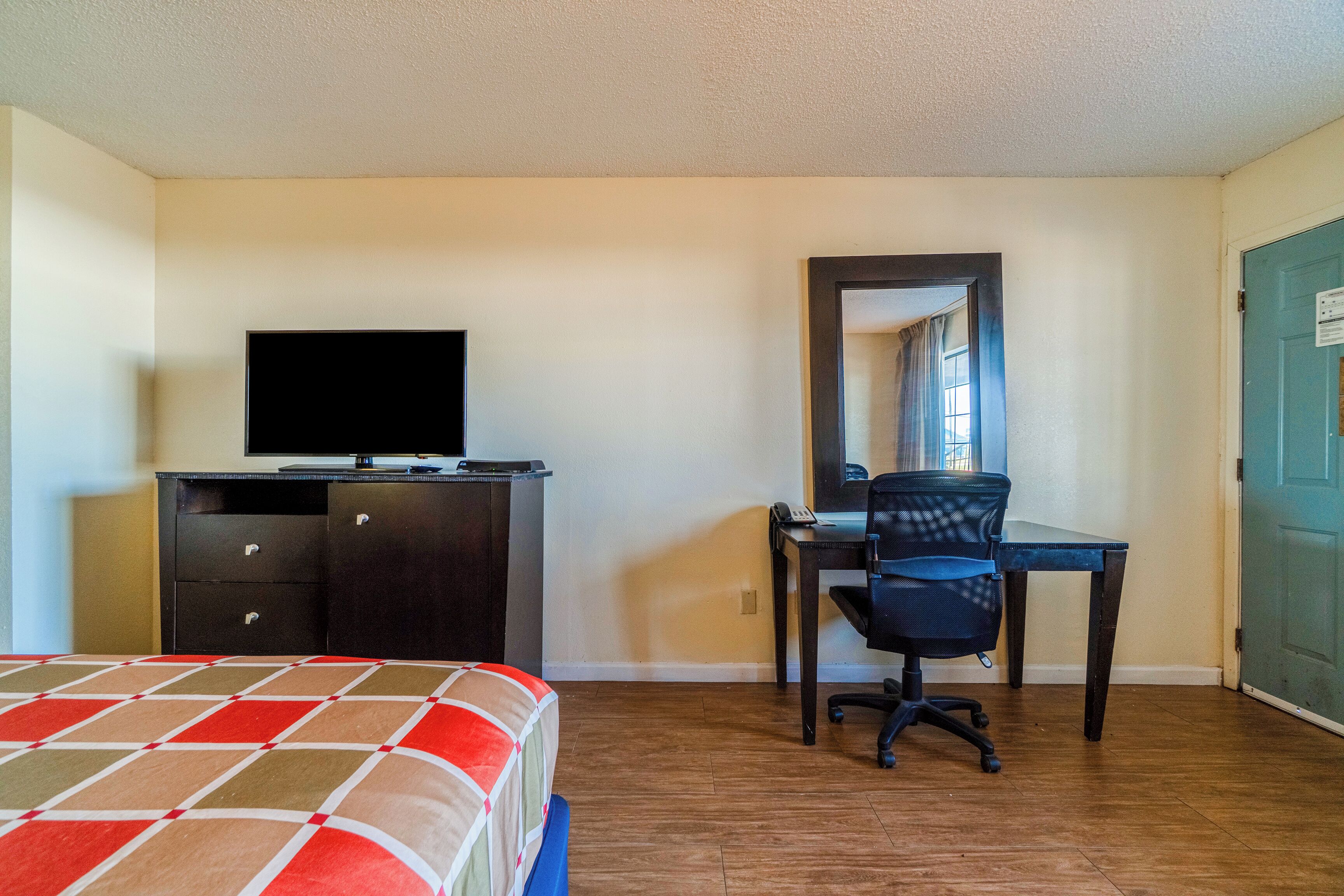 A hotel room with a bed, a desk, a chair, a television, and a wardrobe.