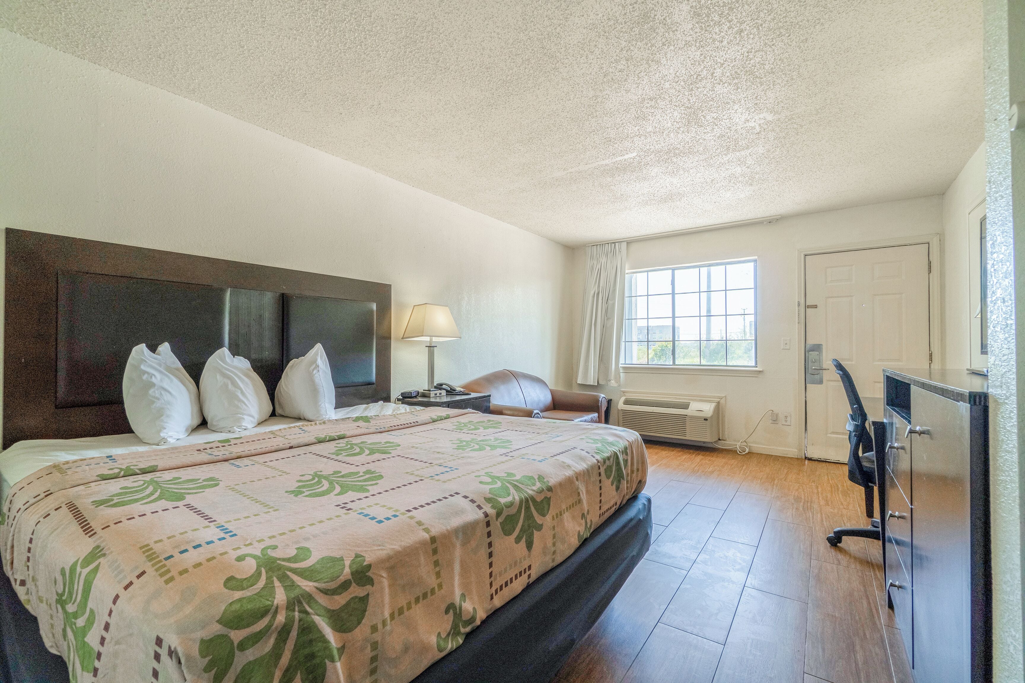 A hotel room with a large bed, a desk, a chair, a window with curtains, and a radiator.