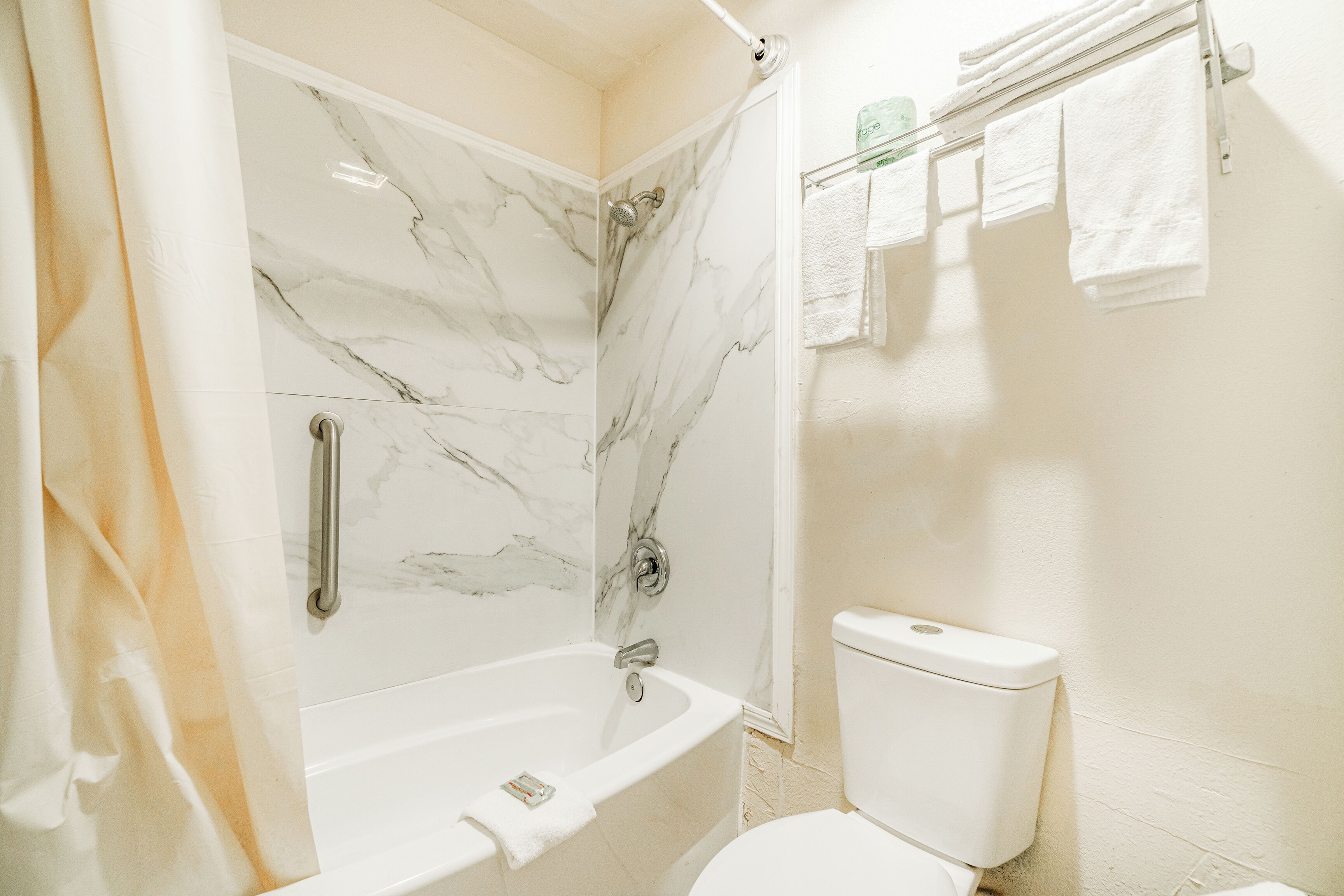 A bathroom with a marble shower, a white toilet, and a towel rack with towels.