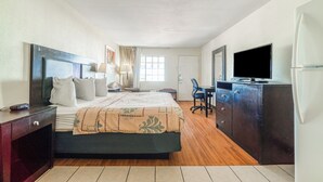 A hotel room with a bed, a desk, a television, and a refrigerator.