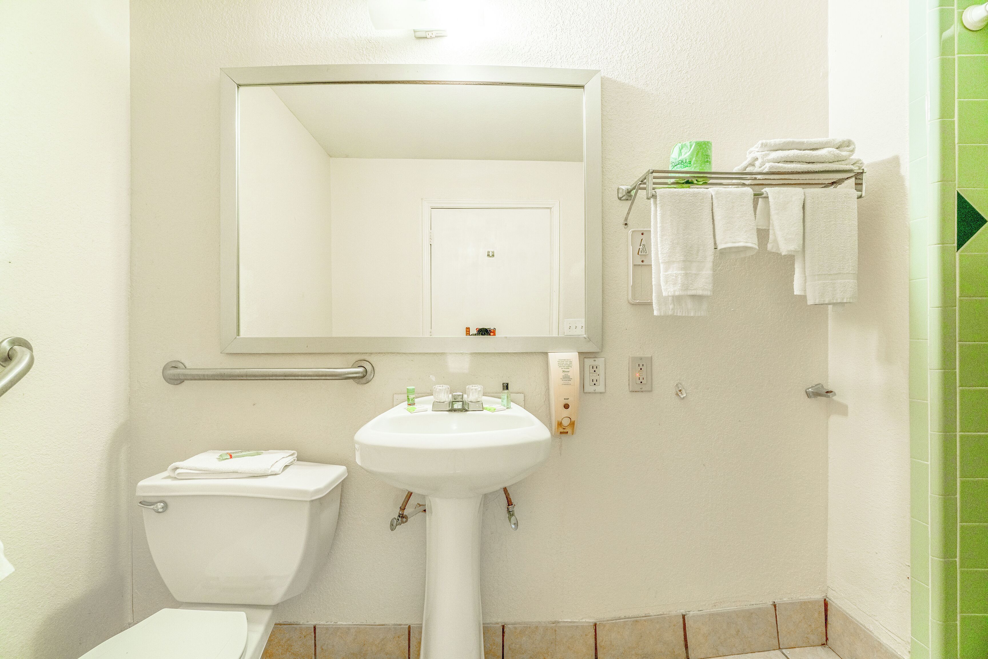 A bathroom with a white sink, a mirror, a toilet, and a towel rack with folded towels.