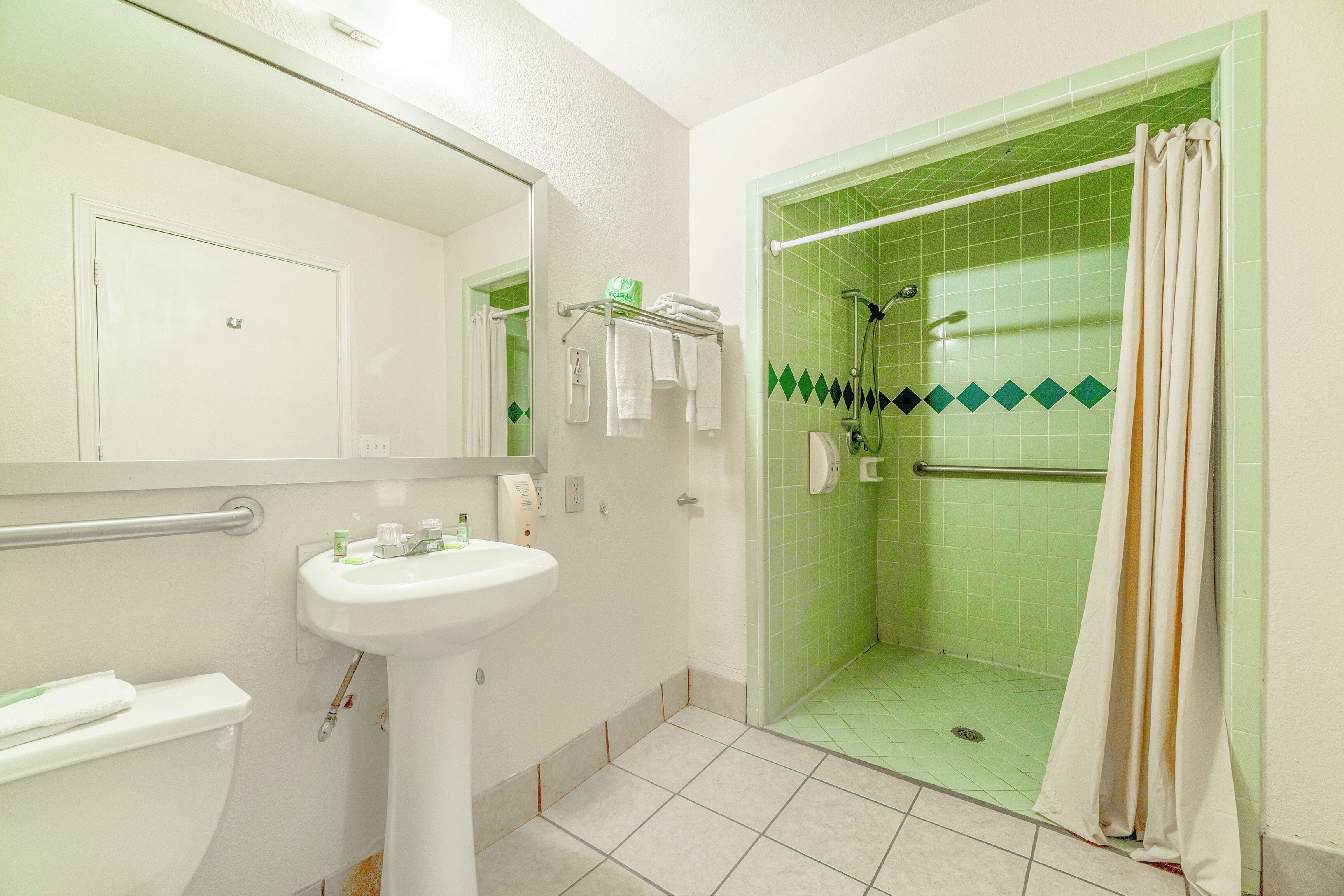 Ein Badezimmer mit weißem Waschbecken, einem Spiegel, einer Toilette und einem Duschen mit grünen Fliesen.