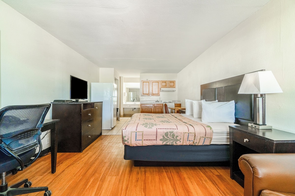 Quarto de hotel com cama, escrivaninha, cadeira e televisão.