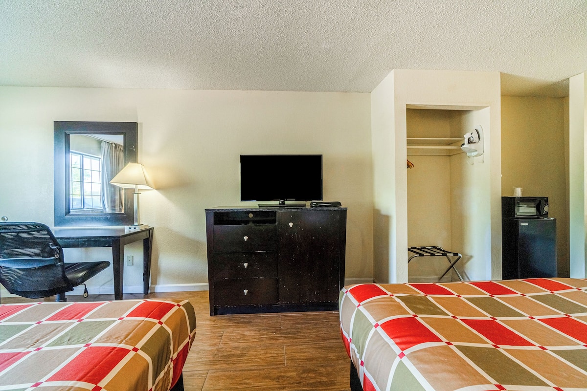 Quarto de hotel com duas camas, uma escrivaninha com cadeira, cômoda, televisão, micro-ondas e armário.