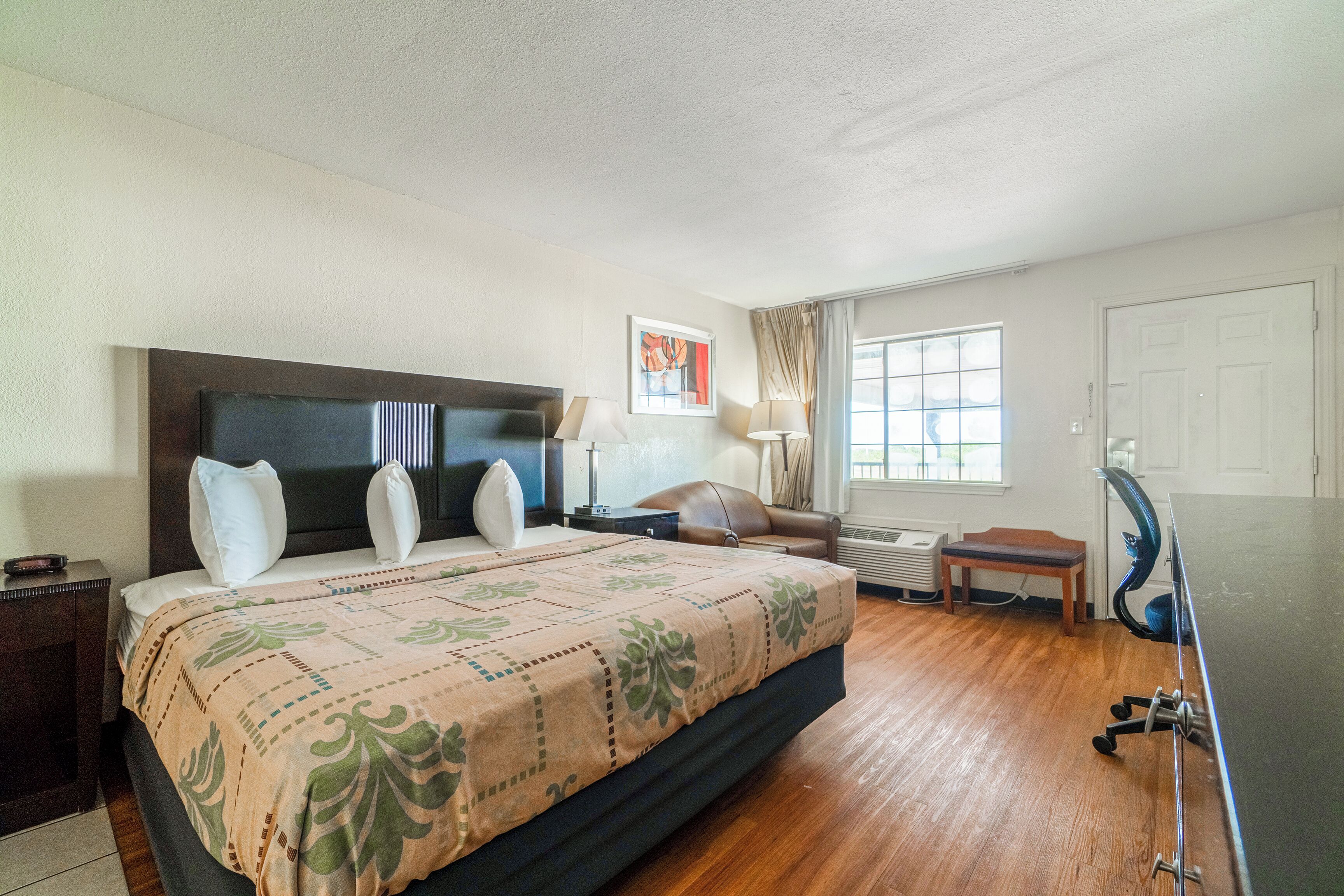 Habitación de hotel con una cama grande, un escritorio, una silla, una ventana con cortinas y una puerta.