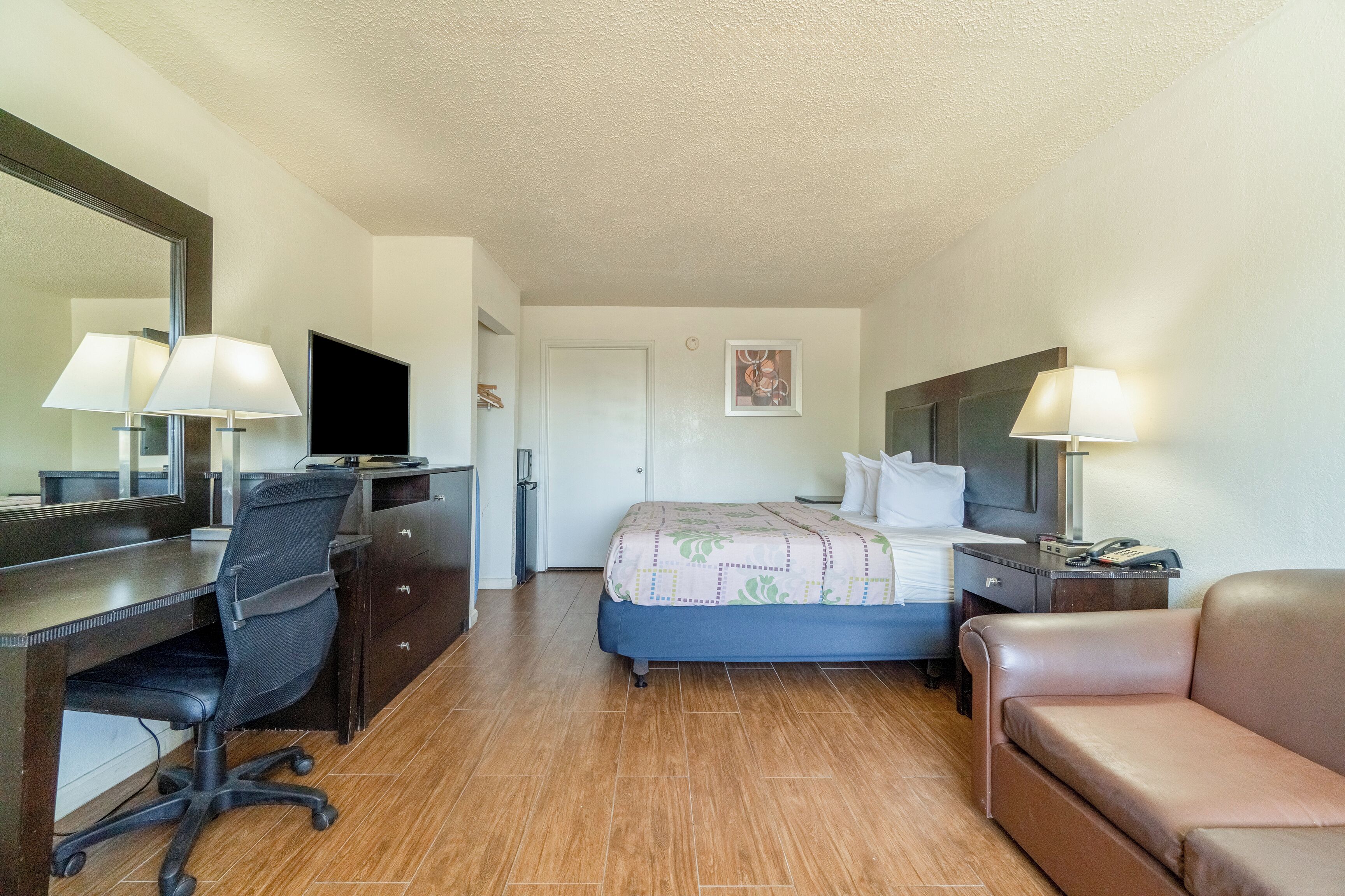 A hotel room with a bed, a desk with a chair, a couch, a TV, and a mirror.