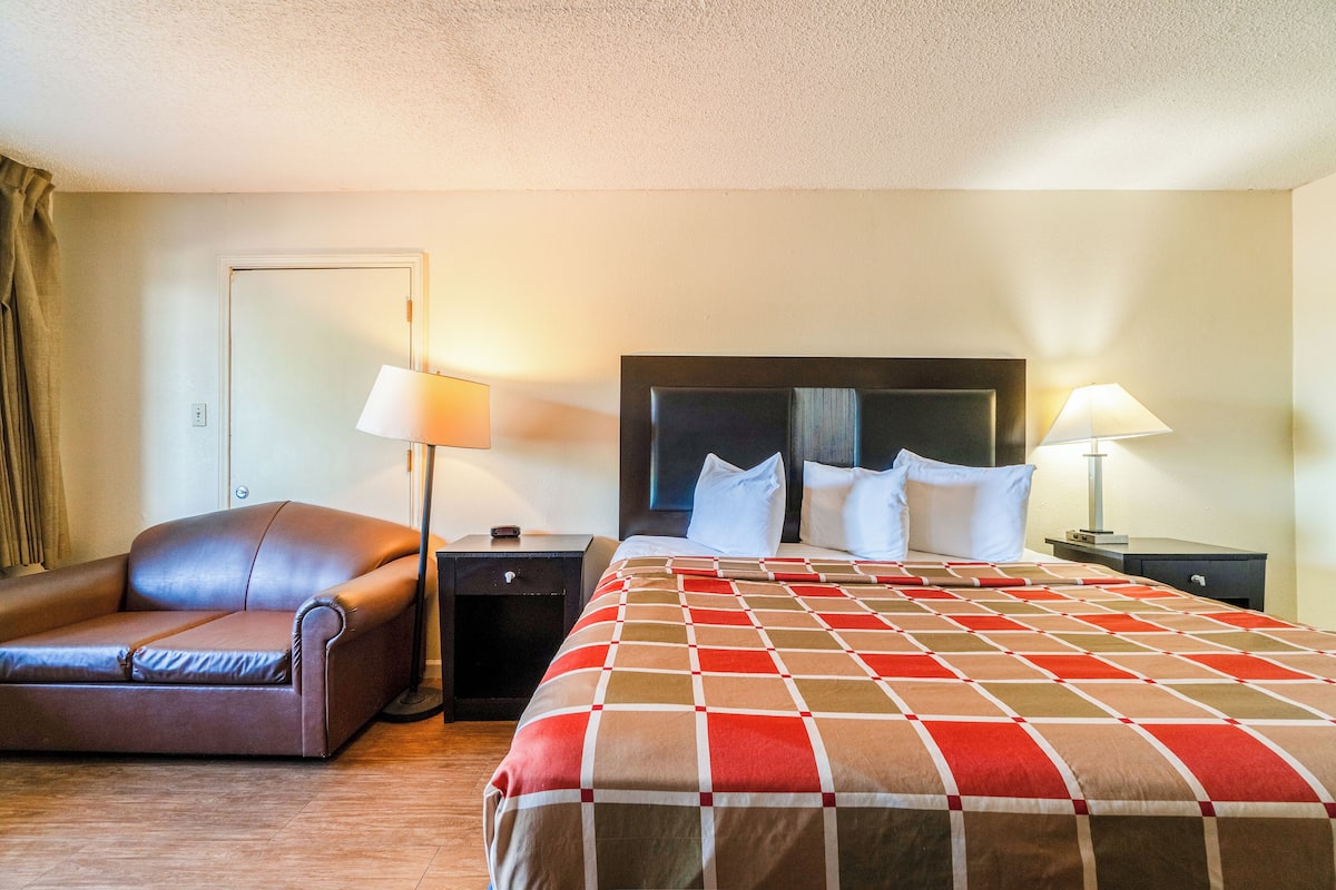 Quarto de hotel com cama, poltrona de couro, duas mesas de cabeceira e duas luminárias.