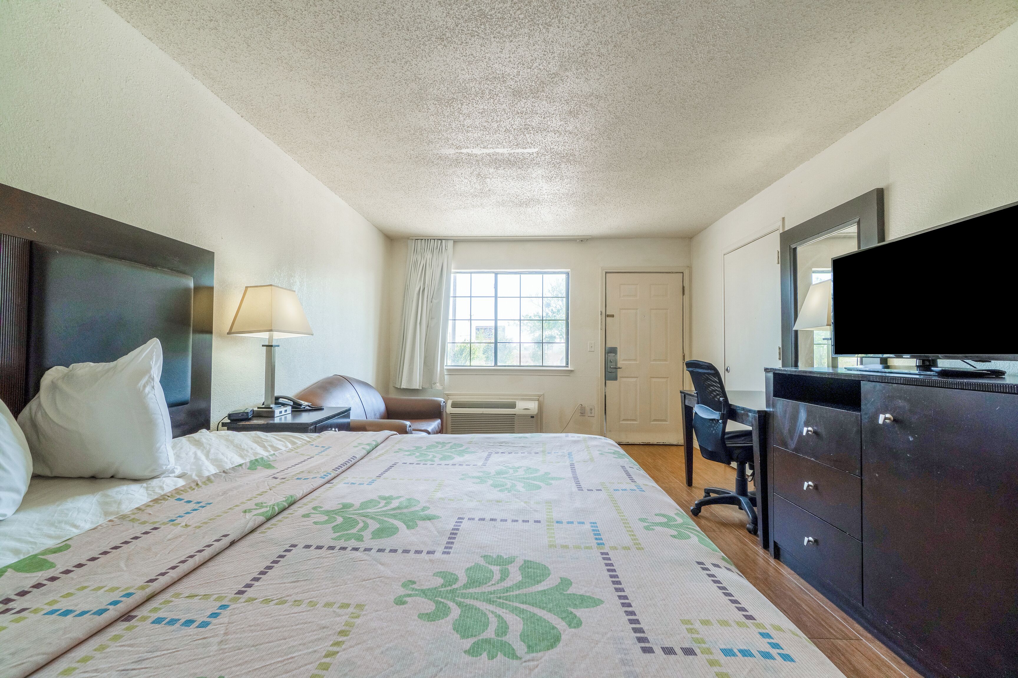 Een hotelkamer met een bed, een bureau, een stoel, een televisie en een raam.
