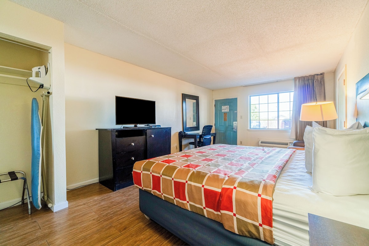 Quarto de hotel com cama, escrivaninha, televisão e janela com cortinas.