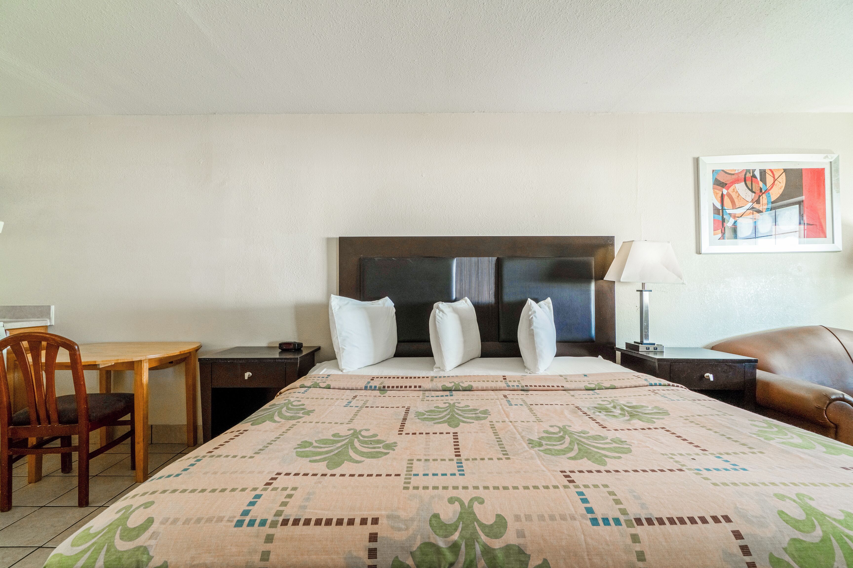A hotel room with a bed, a desk, a chair, a nightstand, and a lamp.