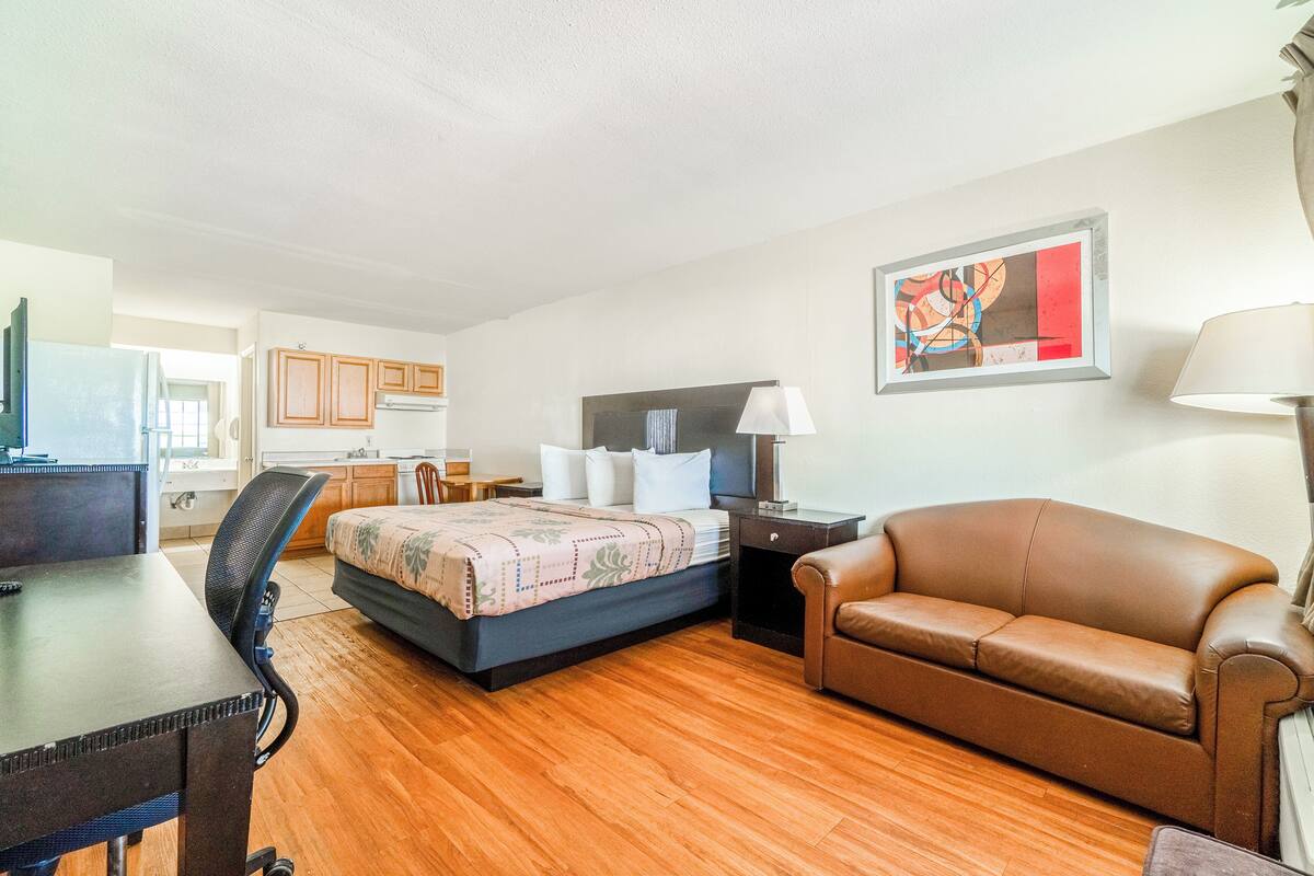 Quarto de hotel com cama, escrivaninha, poltrona, sofá e cozinha.