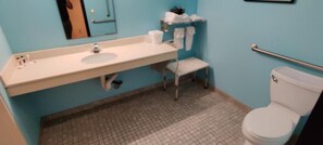 A bathroom with a white sink, mirror, and toilet. There is a small chair and a towel rack. - Super 8 by Wyndham Pennsville/Wilmington (Pennsville)