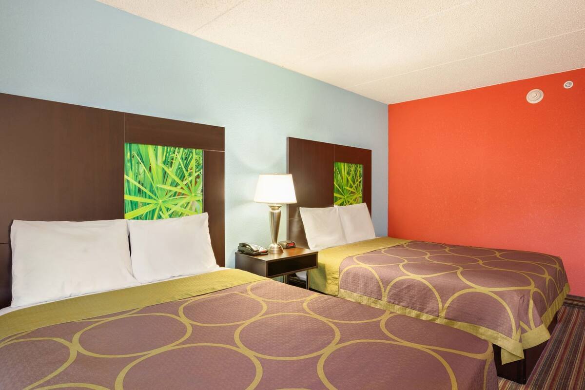 A hotel room with two beds, a nightstand, a lamp, and a wall with a green leafy pattern.
