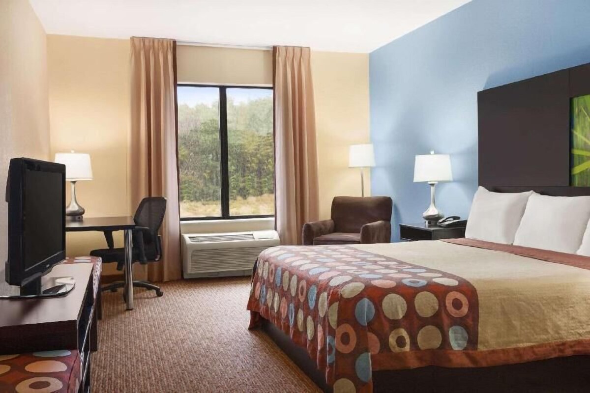 A hotel room with a bed, a desk with a computer, a chair, two lamps, and a window with curtains.
