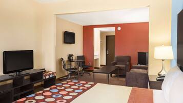 A hotel room with a bed, a desk with a computer, a television, a chair, and a sofa.