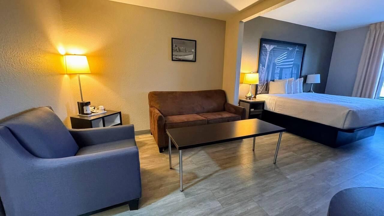 Una habitación de hotel con una cama, un sofá, una mesita de centro y dos lámparas.
