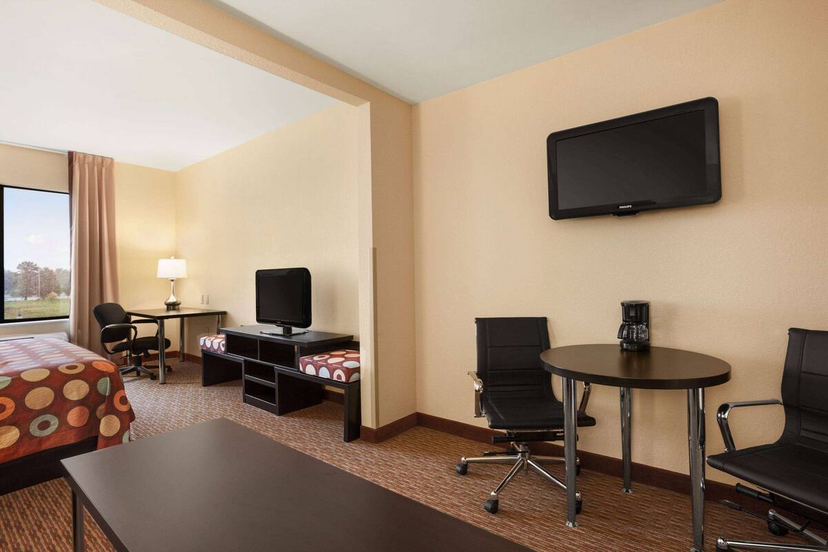 A hotel room with a bed, desk, chairs, a television, and a coffee maker.