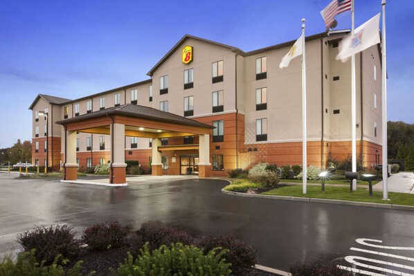 A hotel with a covered entrance, multiple floors, and flags. - Super 8 by Wyndham Pennsville/Wilmington (Pennsville)