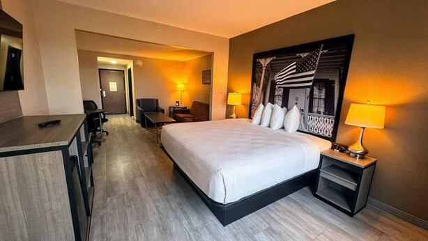 A hotel room with a large bed, a desk with a chair, a small table, and two lamps.