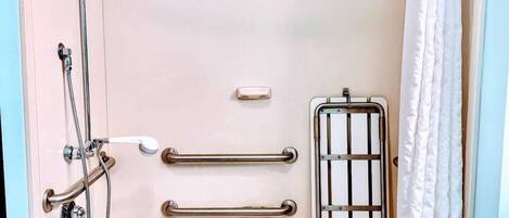 A modern bathroom with a bathtub, shower, and handrails.