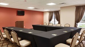A conference room with a long table, chairs, a podium, and a television on the wall.