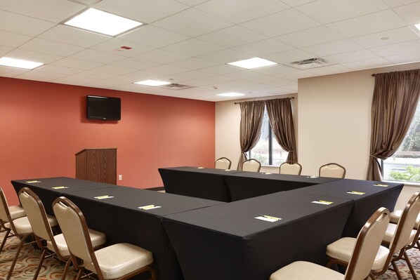 A conference room with a long table, chairs, a podium, and a television on the wall.