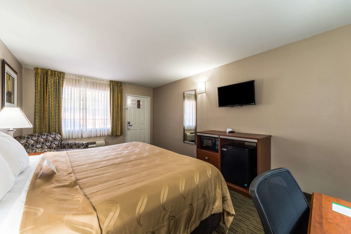 A hotel room with a bed, a desk, a chair, a television, and a window with curtains.