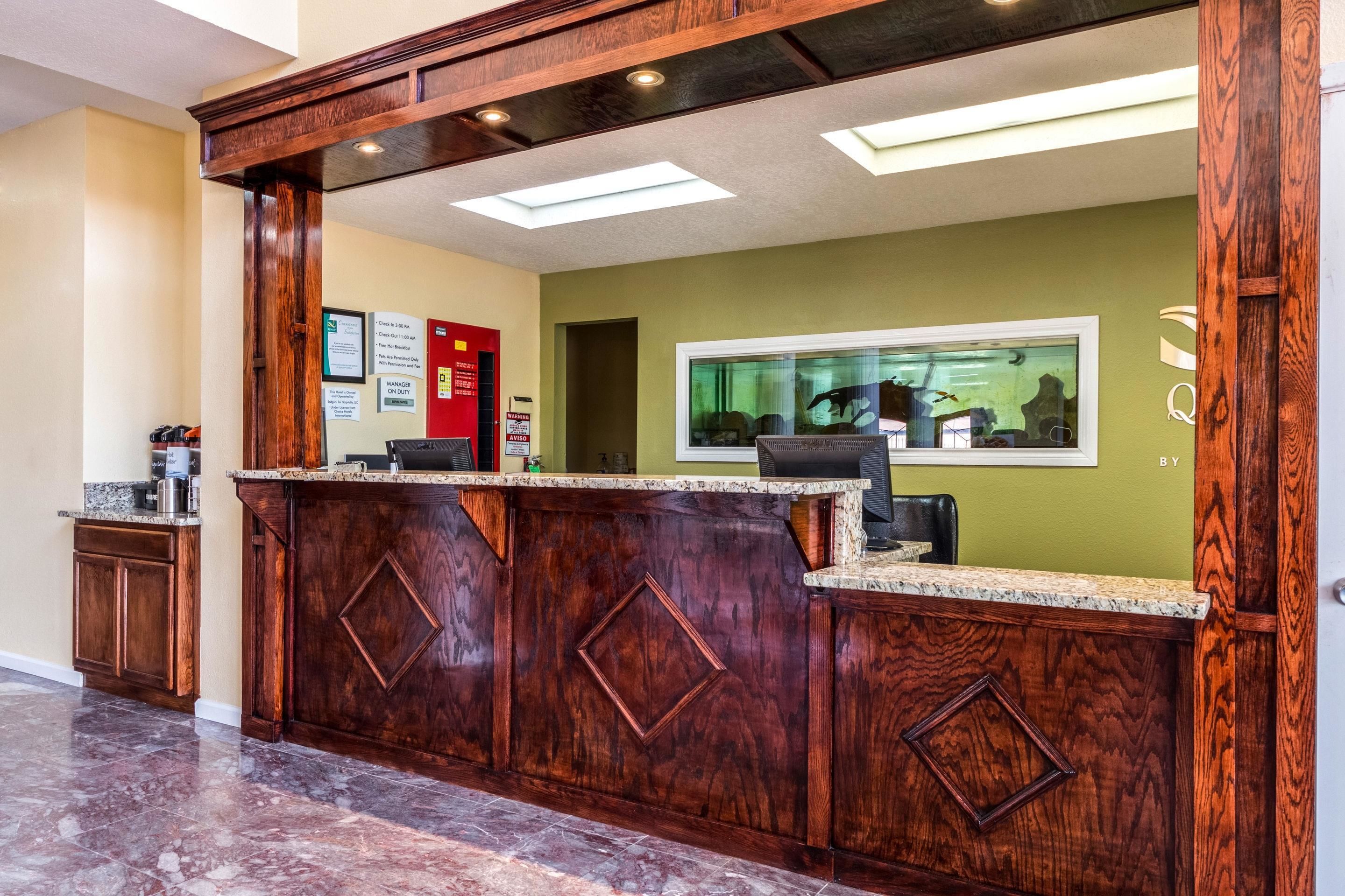 A reception area with a wooden reception desk, a green wall, and a window with a view of the interior.