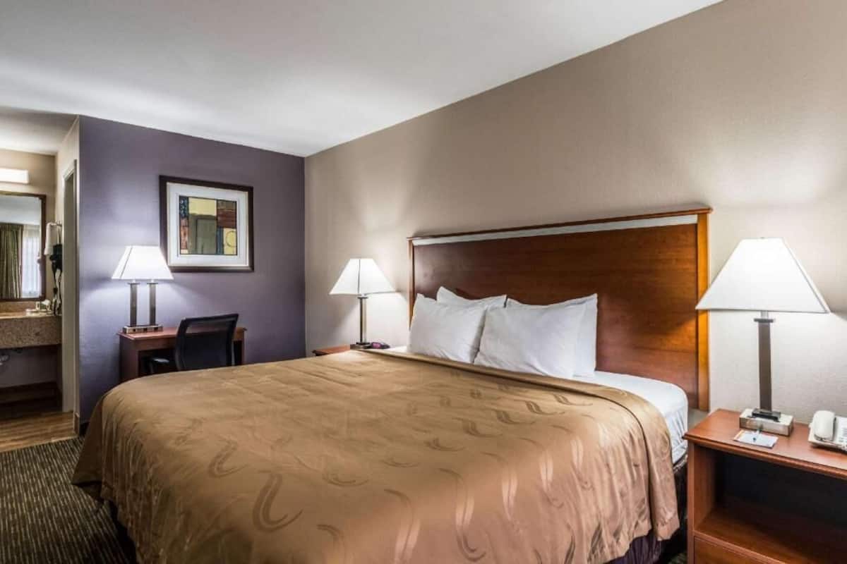 A hotel room with a large bed, two bedside tables with lamps, a desk with a chair, and a mirror.