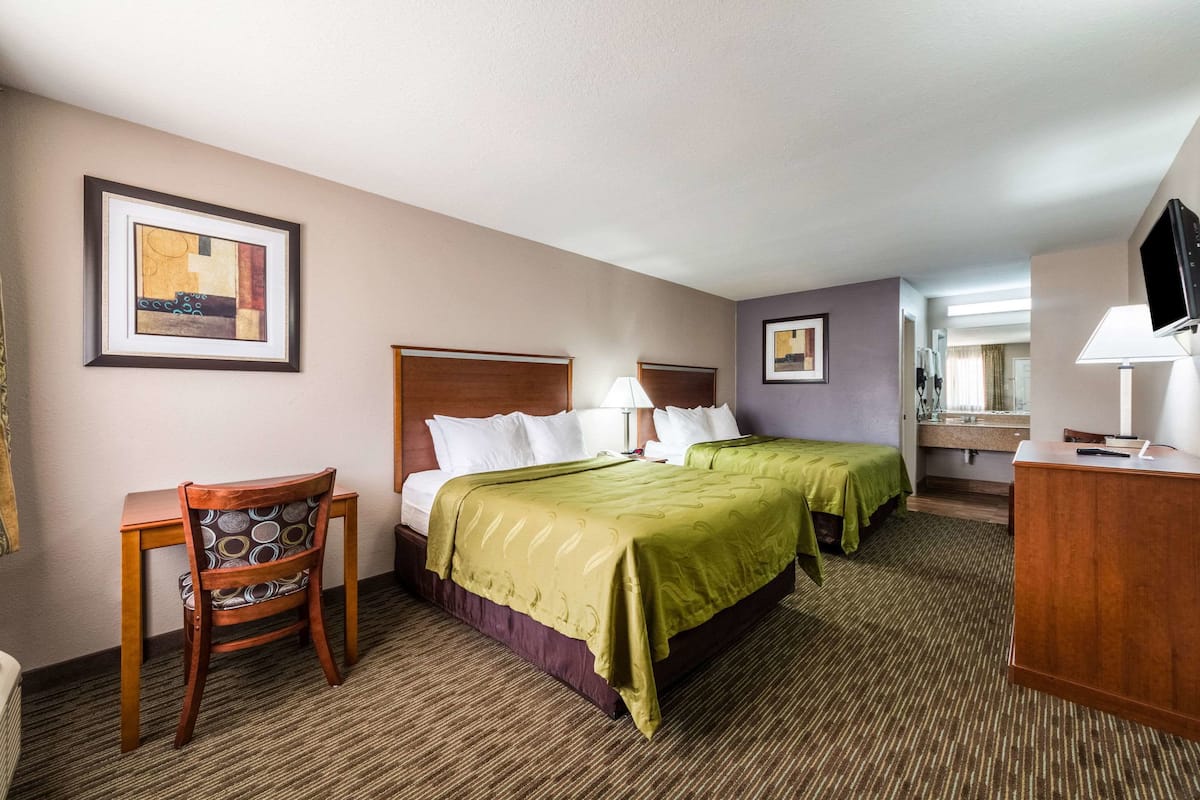 A hotel room with two beds, a desk, a chair, a television, and artwork on the walls.