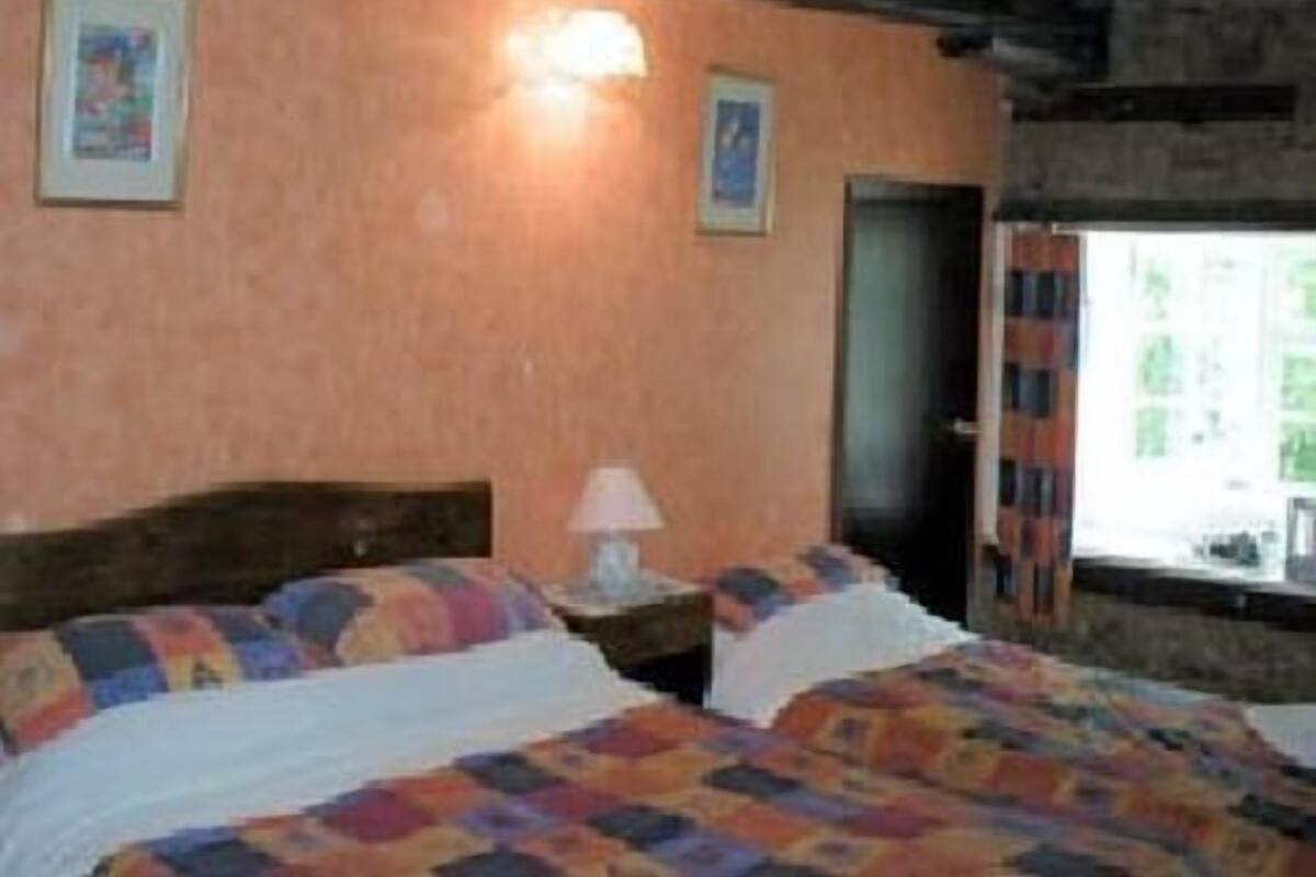 Een slaapkamer met twee bedden, een houten hoofdbord, een nachtkastje met een lamp en ingelijste foto’s aan de muur.