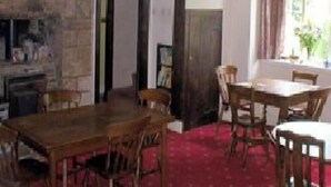 A dining area with a wooden table and chairs, a stone fireplace, and a window with curtains. - Church Farm Guest House (Monmouth)