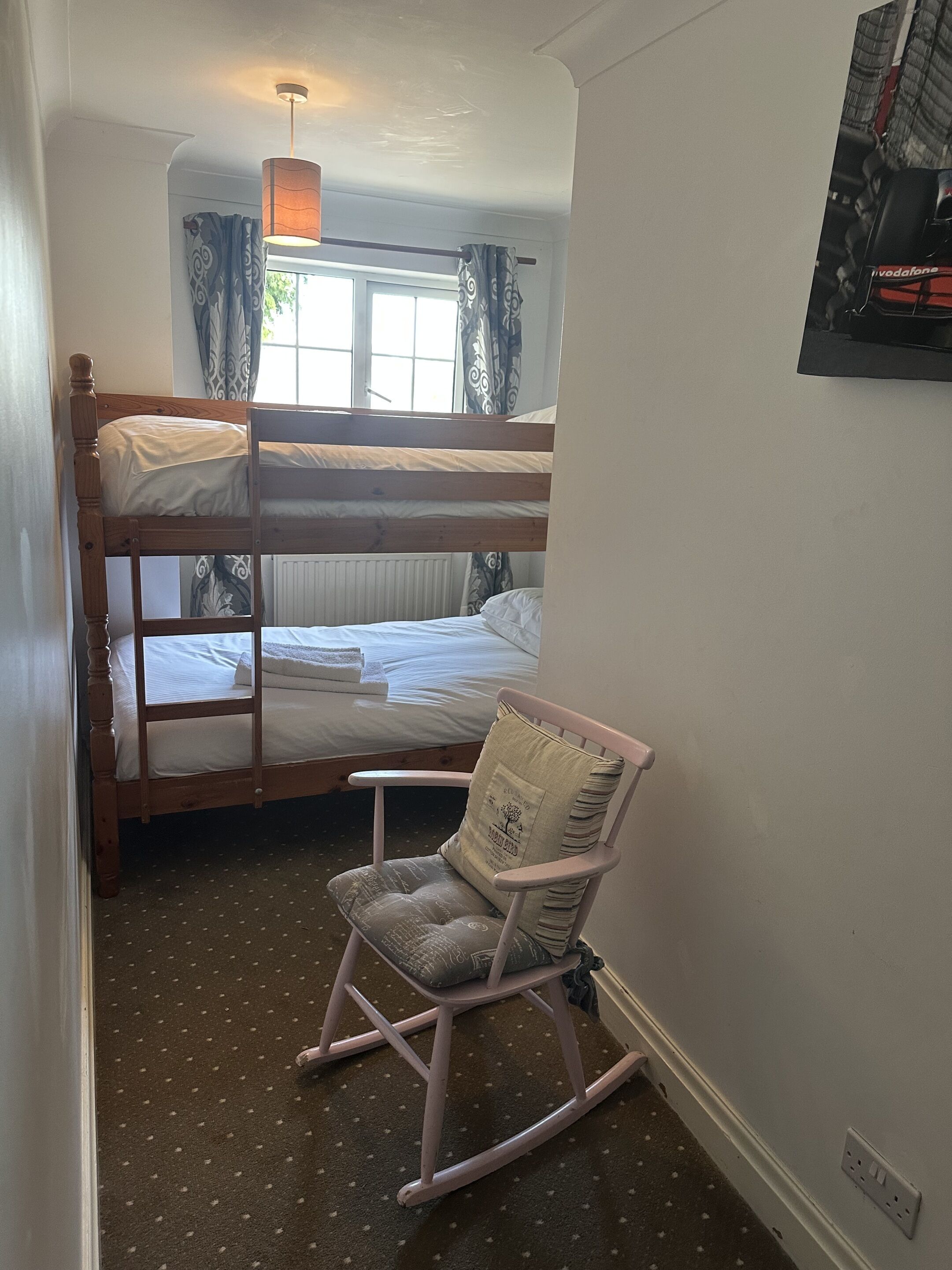 A bunk bed room with a rocking chair, a window with curtains, and a poster on the wall.