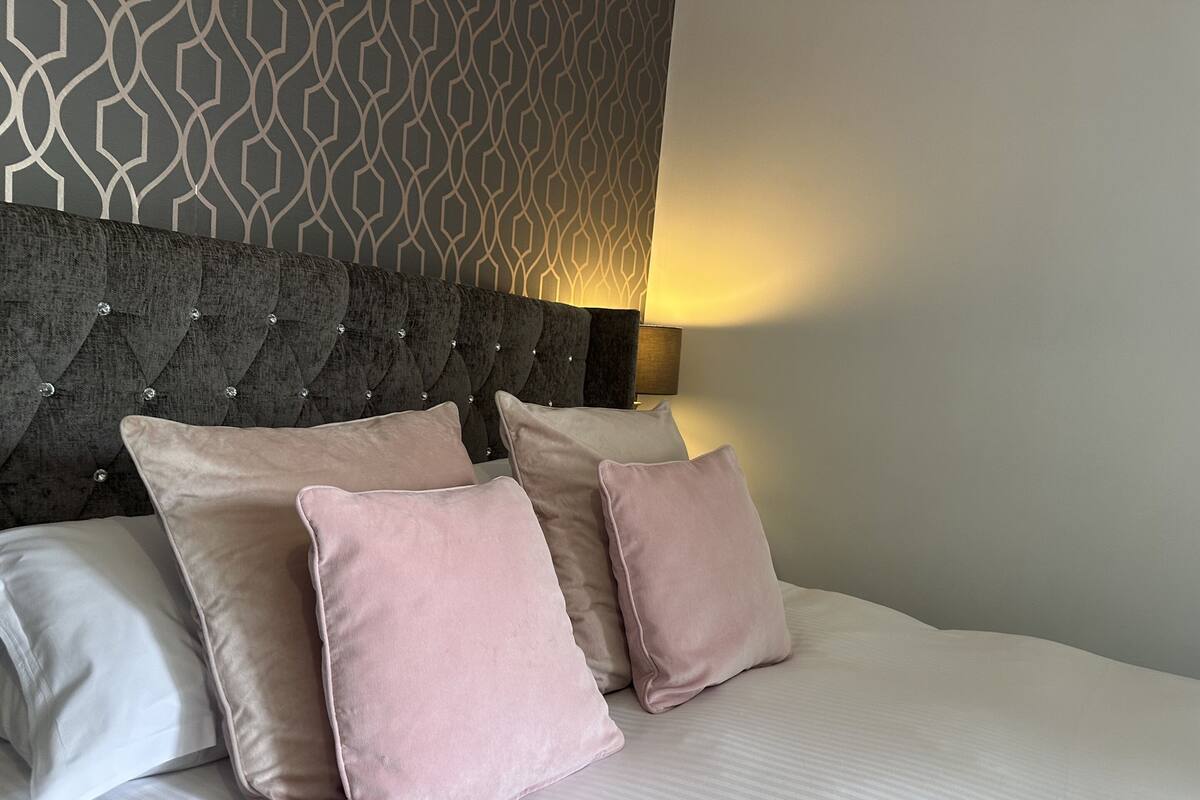 A bed with a tufted headboard, two pillows, and a patterned wall.