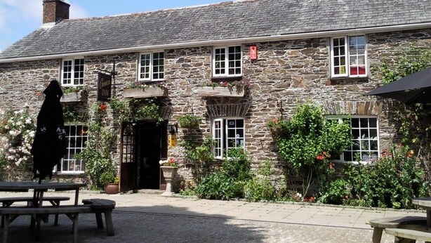 Un bâtiment en pierre avec une enseigne de pub, des fenêtres et des tables à l'extérieur.
