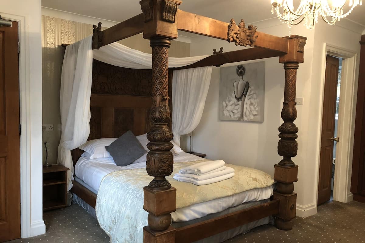 A four-poster bed with a canopy, a chandelier, and a painting on the wall.