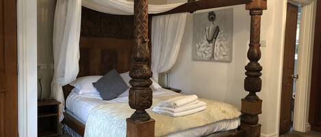 A four-poster bed with a canopy, a chandelier, and a painting on the wall.