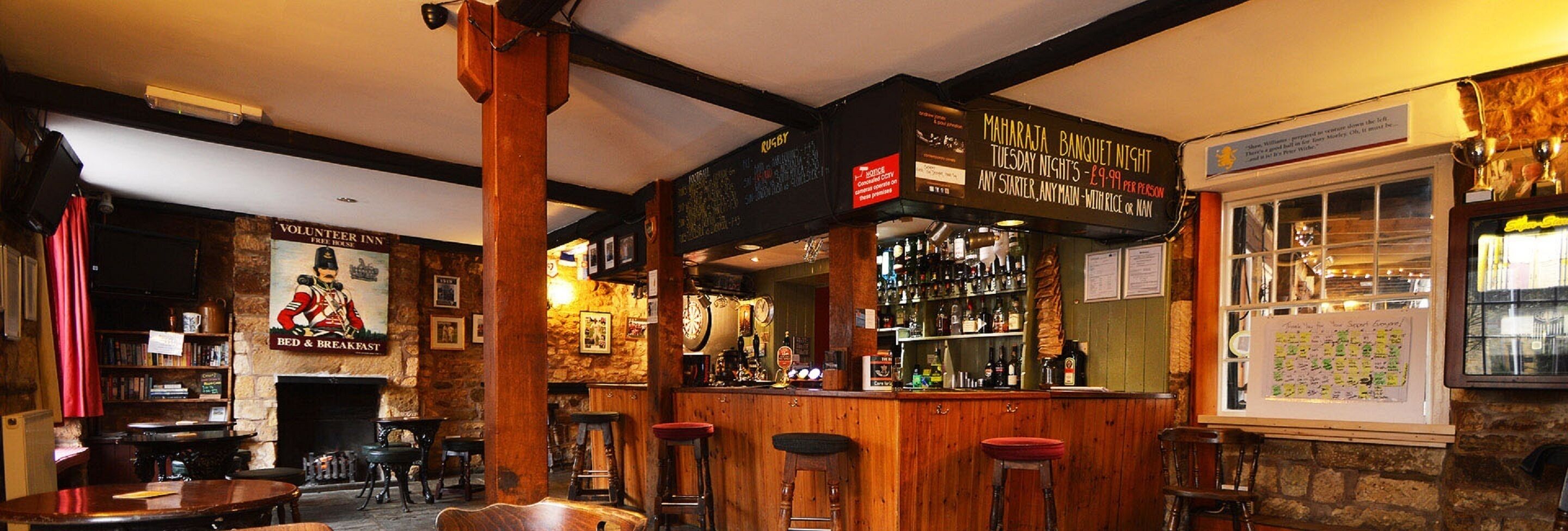 Zona de bar con taburetes de madera, un dardo y un cartel anunciando un partido de rugby.