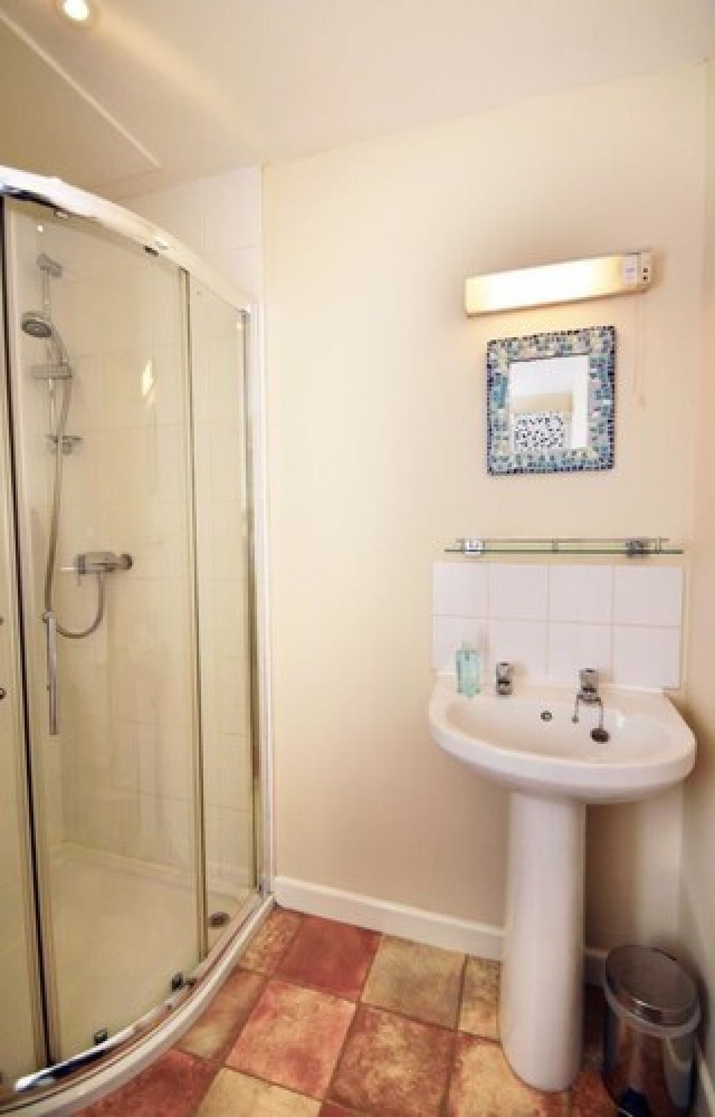 A bathroom with a glass-enclosed shower, a pedestal sink, and a tiled floor.