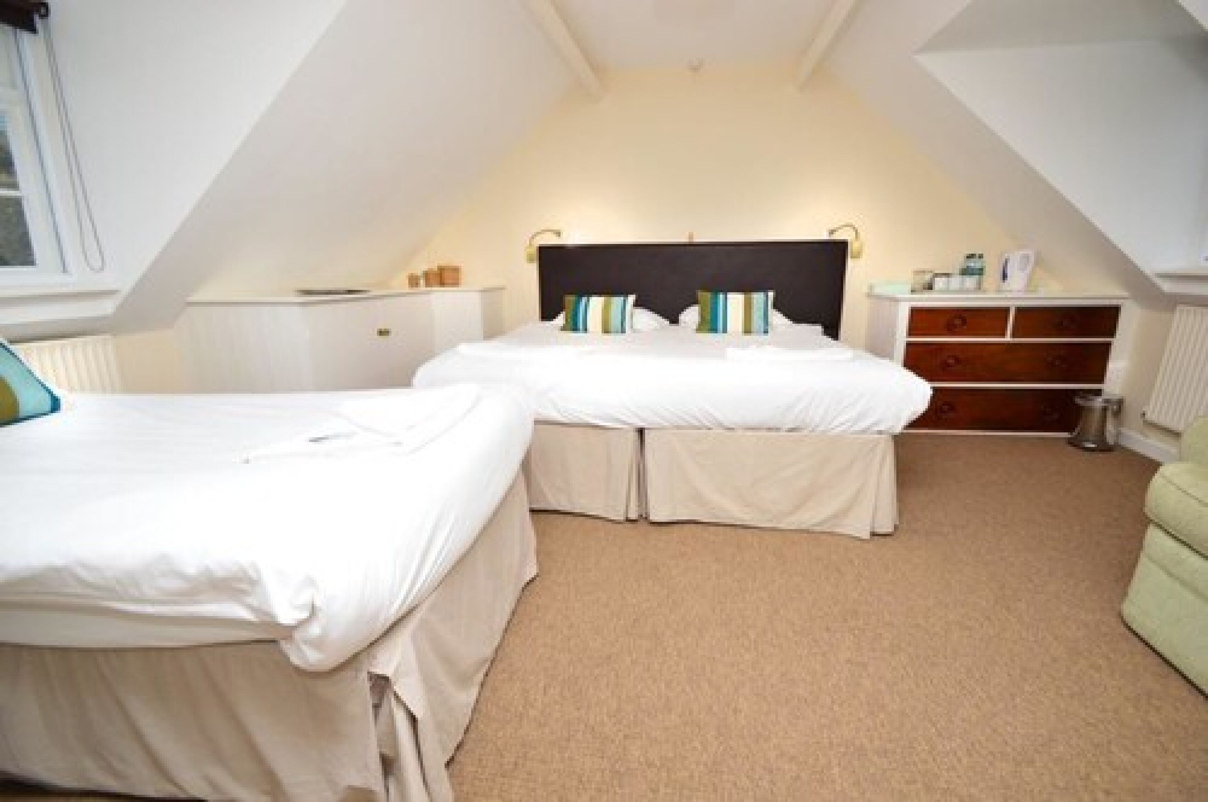 Un dormitorio pequeño y acogedor con dos camas, una mesita de noche y un aparador.