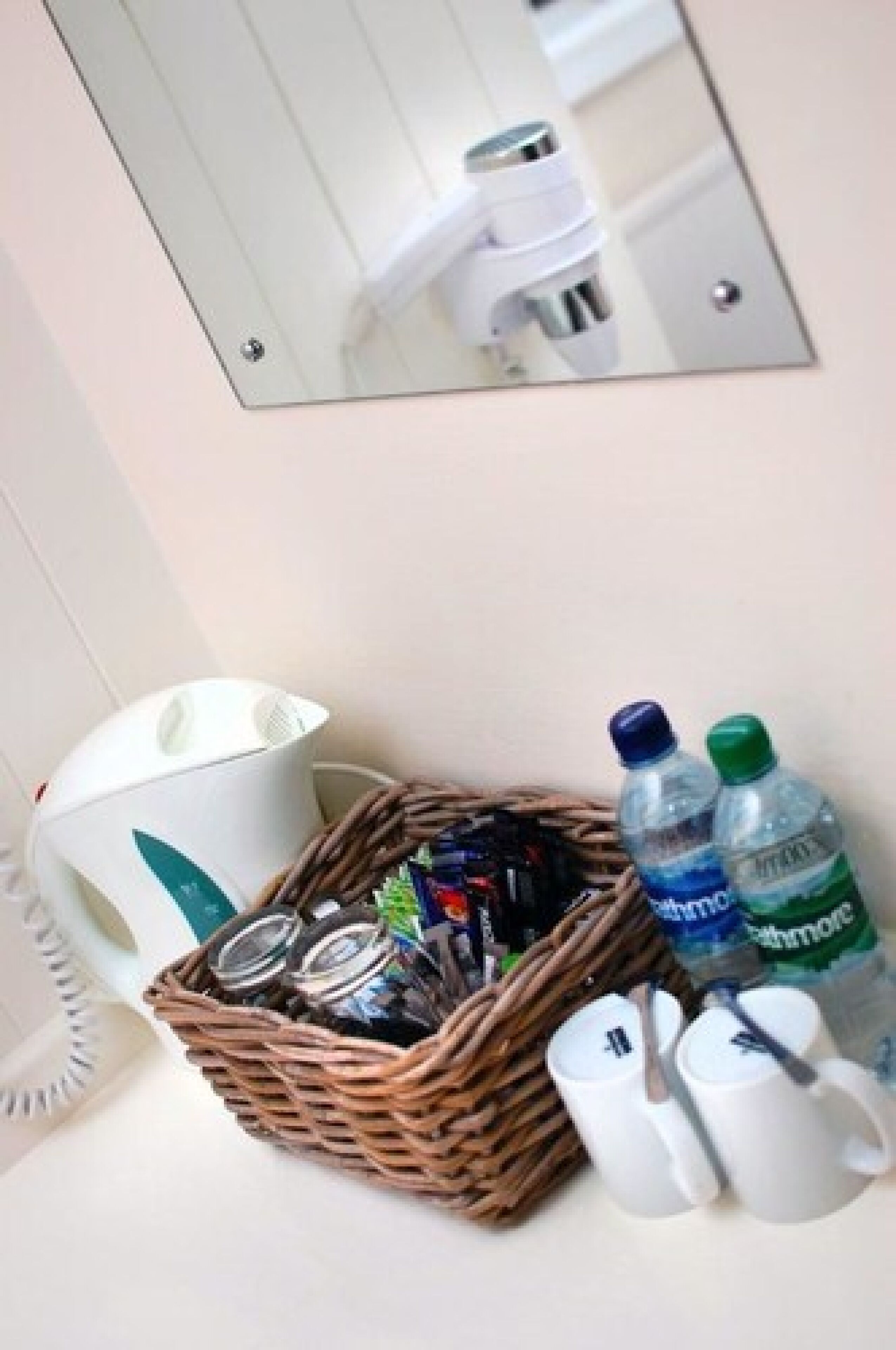 A bathroom with a mirror, a wicker basket with toiletries, and two water bottles.