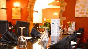 A restaurant interior with tables set for dining, featuring a stone wall and warm lighting.