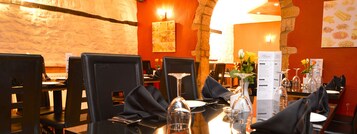 Interior de restaurante con mesas dispuestas para comer, destacando una pared de piedra e iluminación cálida.