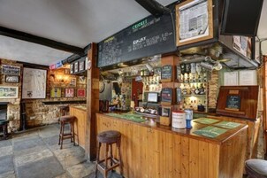 Un bar con mostradores y taburetes de madera, un menú en la pizarra y diversas botellas y vasos.