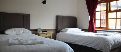 Une chambre d’hôtel avec deux lits, une table de chevet, une lampe et une fenêtre avec des rideaux.